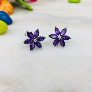 May include: A pair of silver flower-shaped earrings with purple gemstones and a small clear gemstone in the center of each flower.
