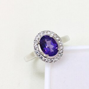 Peut inclure: Une bague en argent avec une grande améthyste ovale entourée d'un halo de petites pierres précieuses claires.