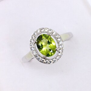 Peut inclure: Une bague en argent avec une pierre ovale verte entourée d'un halo de petites pierres blanches.