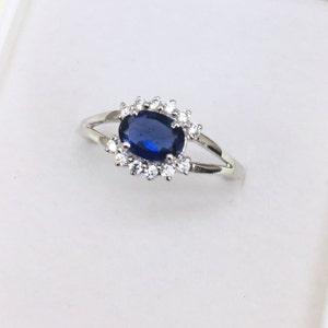 Peut inclure: Une bague en argent avec une pierre précieuse ovale bleue entourée de petites pierres blanches.
