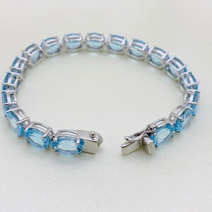 May include: A silver bracelet with a clasp closure, featuring a row of oval-shaped blue gemstones.