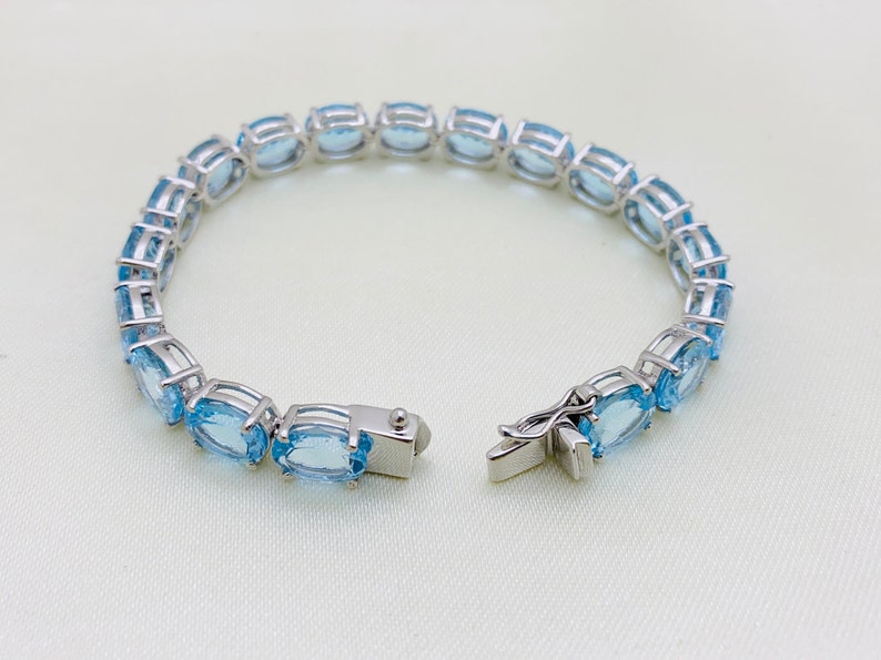 May include: A silver bracelet with a clasp closure, featuring a row of oval-shaped blue gemstones.