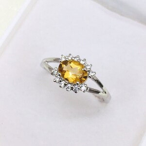 Peut inclure: Une bague en argent avec une pierre ovale jaune entourée de petites pierres claires.