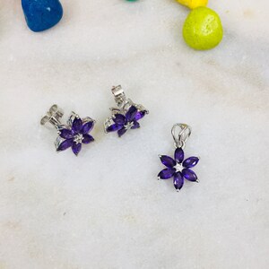 May include: A set of amethyst flower earrings and a matching pendant necklace. The earrings and pendant are made of silver and feature a cluster of purple amethyst stones in the shape of a flower.