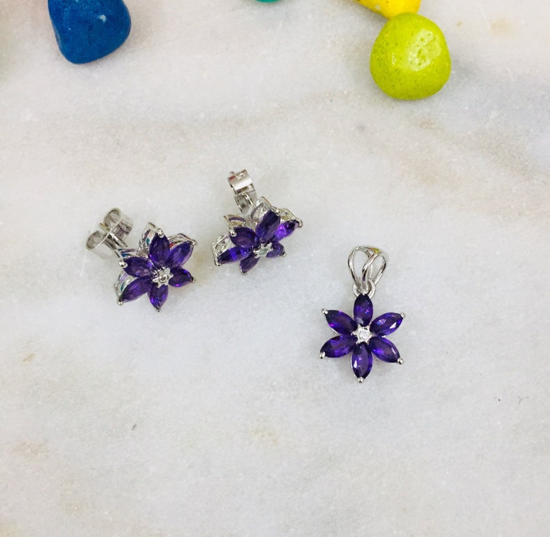 May include: A set of amethyst flower earrings and a matching pendant necklace. The earrings and pendant are made of silver and feature a cluster of purple amethyst stones in the shape of a flower.
