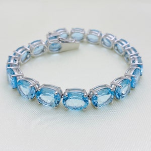 May include: A silver bracelet with a row of oval-shaped blue topaz gemstones.
