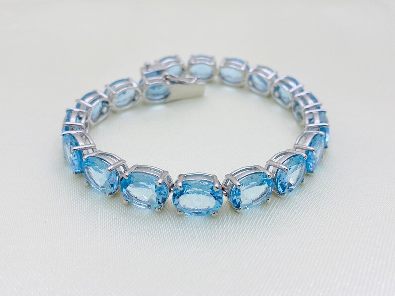May include: A silver bracelet with a row of oval-shaped blue topaz gemstones.