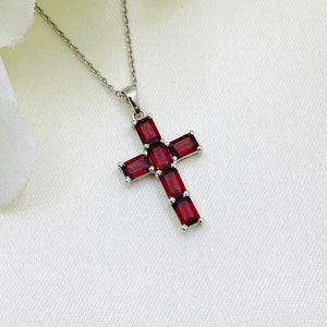 Könnte beinhalten: Eine silberne Halskette mit einem roten Edelstein-Kreuzanhänger. Das Kreuz besteht aus mehreren rechteckigen roten Edelsteinen.