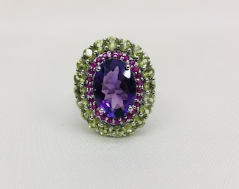 May include: A silver ring with a large oval amethyst gemstone surrounded by a halo of smaller green and pink gemstones.