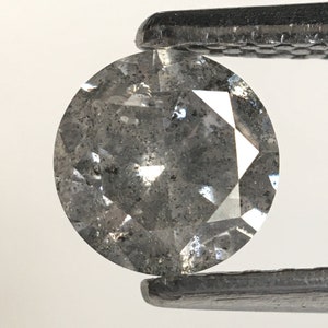 May include: A round, gray diamond with a faceted cut. The diamond is held in tweezers and has a cloudy appearance.