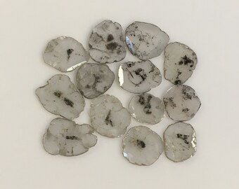 May include: A collection of 12 clear quartz crystal slices with black inclusions. The slices are irregularly shaped and have a natural, raw look.
