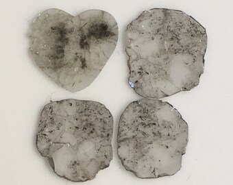 May include: Four clear glass coasters with a gray, speckled, and slightly cloudy appearance. The coasters are in the shape of a heart and two ovals.