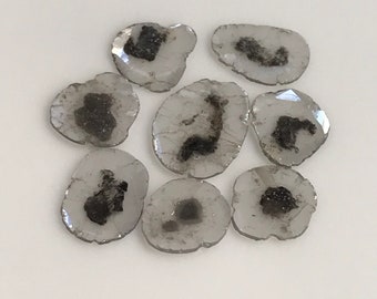 May include: A collection of eight clear, faceted, quartz crystals with black inclusions. The crystals are oval shaped and have a natural, raw look.