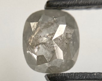 May include: A gray, cushion-cut diamond with a rough, natural finish. The diamond is held by tweezers.
