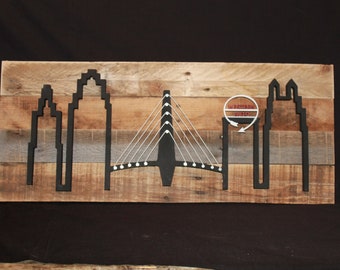 May include: A wooden wall art piece featuring a black silhouette of a city skyline with a bridge and the text "LA BOUCHERE" in a red circle with a white arrow.