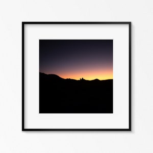 Könnte beinhalten: Ein schwarz gerahmtes Foto eines Sonnenuntergangs über einem Gebirge. Der Himmel ist ein Farbverlauf von Lila, Rosa und Orange. Die Berge sind vor dem Himmel silhouettiert.