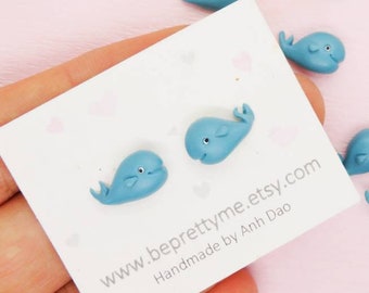May include: A hand holding a card with the text "www.beprettyme.etsy.com Handmade by Anh Dao" and nine blue whale figurines on a pink background.