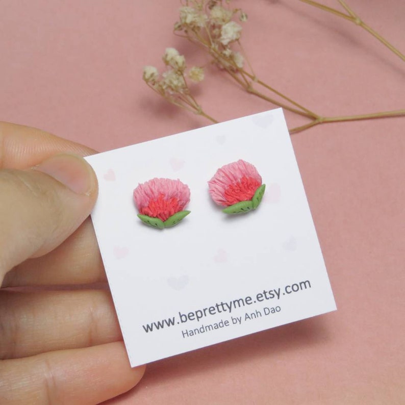 May include: A pair of pink and green flower stud earrings. The earrings are handmade and feature a small, delicate flower design. The earrings are on a white card with the text "www.beprettyme.etsy.com Handmade by Anh Dao."