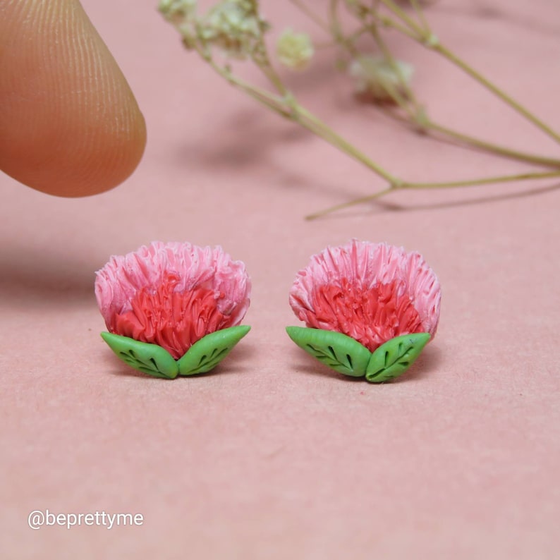 May include: A pair of pink and red flower earrings with green leaves. The earrings are made of polymer clay and are handmade.