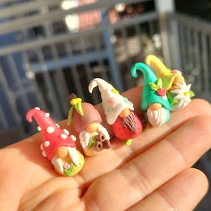 May include: Five miniature gnome figurines made of polymer clay. Each gnome has a different colored hat and a unique design. The gnomes are arranged in a row on a hand.