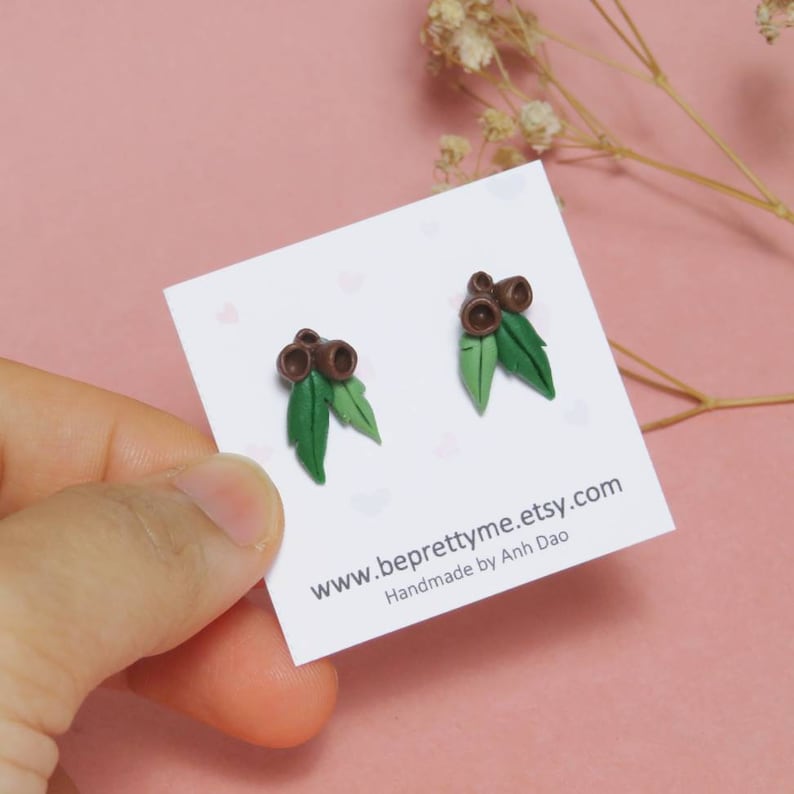 May include: A pair of small, green and brown earrings shaped like gum nuts and leaves. The earrings are on a white card with the text "www.beprettyme.etsy.com Handmade by Anh Dao".