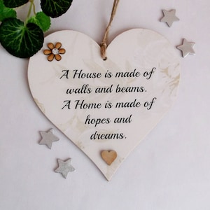 May include: A white wooden heart-shaped sign with a marbled texture and the text "A House is made of walls and beams. A Home is made of hopes and dreams."