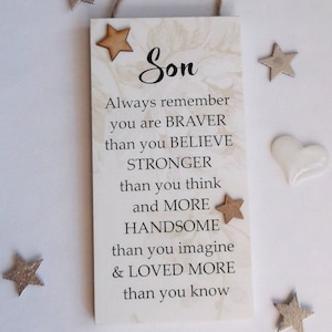 May include: A rectangular wooden plaque with the word "Son" and an inspirational message. The plaque has a marbled background, wooden star accents, and a jute string for hanging. Decorative silver stars and a white heart are scattered around the plaque.