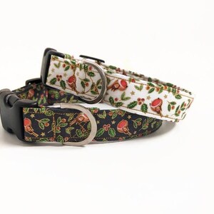May include: Two Christmas-themed dog collars. One collar is white with red robins, green leaves, and red berries. The other is black with the same design. Both have black plastic buckles and silver metal D-rings.