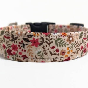 May include: A beige dog collar with a floral pattern featuring red, orange, and green flowers. The collar has a black plastic buckle.
