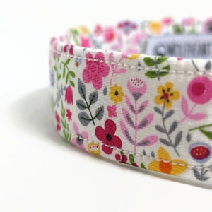 May include: White fabric collar with a floral pattern featuring pink, red, yellow, and green flowers. The collar has a white stitched seam.