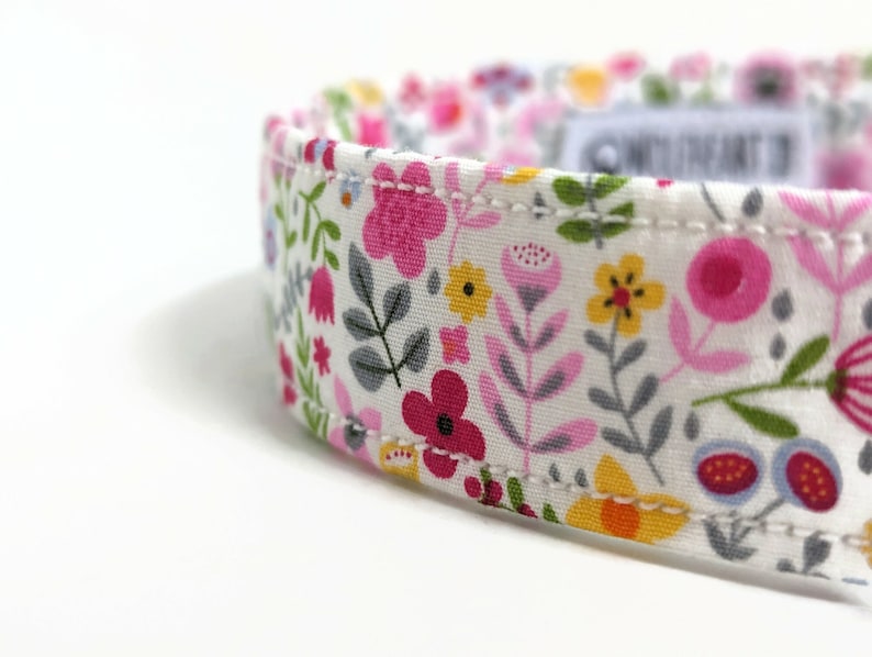 May include: White fabric collar with a floral pattern featuring pink, red, yellow, and green flowers. The collar has a white stitched seam.