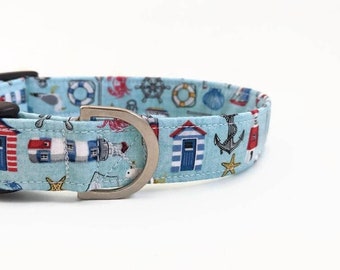 Puede incluir: Un collar para perro azul claro con un estampado de temática náutica que incluye faros, anclas, conchas marinas y casas de playa. El collar tiene una hebilla de metal plateado.