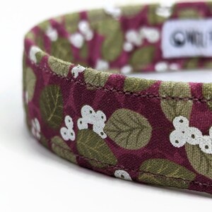 May include: A close-up of a pink and green patterned dog collar with white flowers. The collar is made of fabric and has a stitched seam. The text "One Heart at a Time" is visible on the collar.