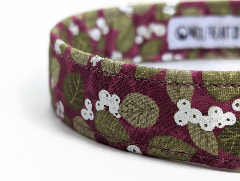 May include: A close-up of a pink and green patterned dog collar with white flowers. The collar is made of fabric and has a stitched seam. The text "One Heart at a Time" is visible on the collar.