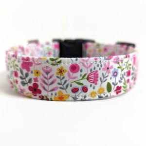 May include: White dog collar with a floral print featuring pink, yellow, and green flowers. The collar has a black plastic buckle.