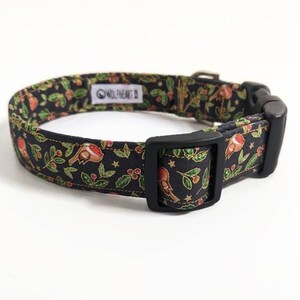 May include: Black dog collar with a festive pattern of birds, berries, and leaves. The collar has a black plastic buckle and a metal adjustment piece. The brand name "WOLFHEART" is visible on a white tag.