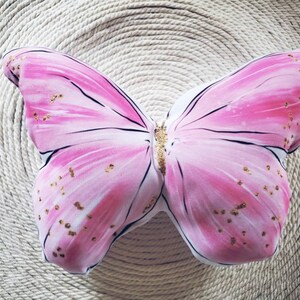 Photo of a pink butterfly shaped pillow, with gold glitter dotted throughout the pillow. Exquisite accent pillow.