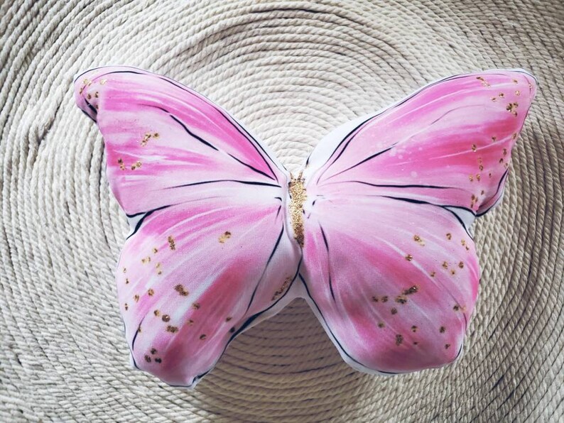 Photo of a pink butterfly shaped pillow, with gold glitter dotted throughout the pillow. Exquisite accent pillow.