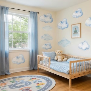 May include: A bedroom featuring light beige walls decorated with multiple watercolour-style blue cloud wall decals. The room includes a wooden toddler bed with blue striped bedding, a wooden toy shelf, a round rug with a road pattern, and blue curtains.
