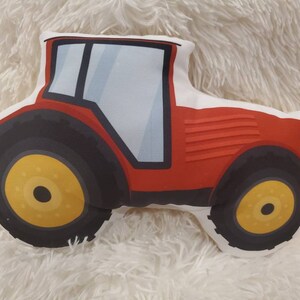 May include: Red tractor-shaped cushion with black wheels and yellow rims. The cushion is made of soft fabric and is ideal for a child's room.