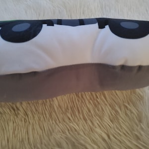 May include: A white and gray pillow with a cartoon car design. The car has black wheels and a green roof.