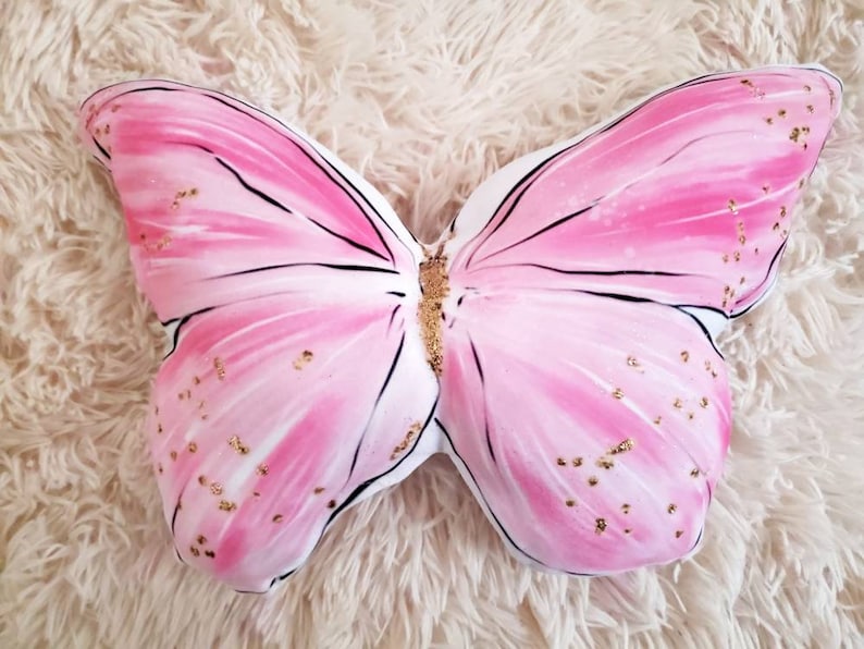 Stunning Butterfly shaped pillow in a soft pink. This is a butterfly throw pillow made using a beautiful illustration of a butterfly, which is hand sewn and stuffed. Gold glitter dots the entire Butterfly pillow for a gorgeous effect.