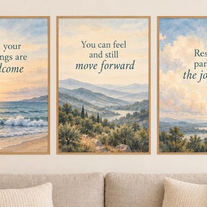 May include: A set of three framed landscape prints with light wood frames. The left print shows a beach at sunset with the text All your feelings are welcome. The center print depicts rolling hills with the text You can feel and still move forward. The right print shows a valley with the text Rest is part of the journey.