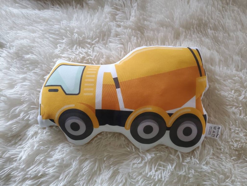 May include: A yellow and orange cement truck plush toy with black wheels and a white outline. The toy is designed with a cartoonish style and is set against a fluffy white background.