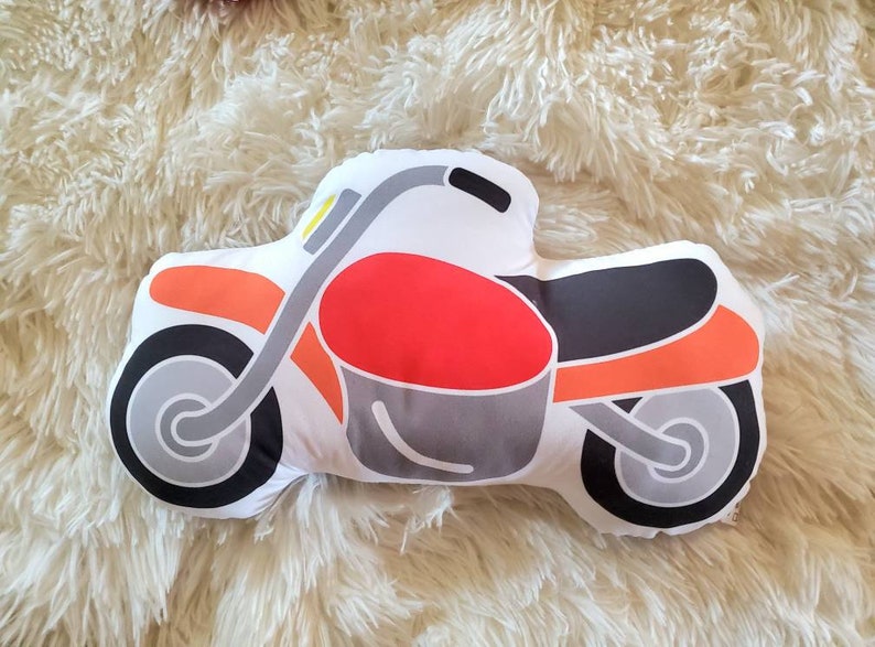May include: A red, orange, black, and gray motorcycle pillow. The pillow is shaped like a motorcycle and has a white background.