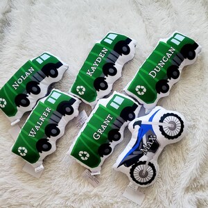 May include: Six green and white plush toy garbage trucks with different names on each truck.  The names are Nolan, Walker, Kayden, Grant, Duncan, and Max.  There is also a blue and white plush toy dirt bike with the name Max on it.