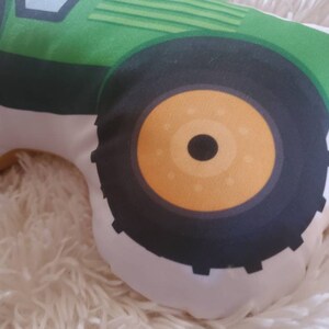 May include: A green and black tractor pillow with a white background. The tractor has a large front tyre with a yellow centre.