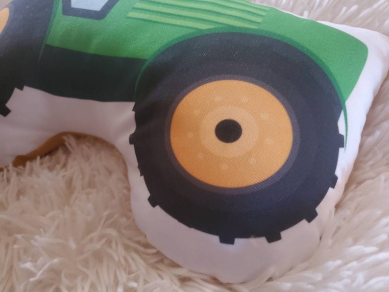 May include: A green and black tractor pillow with a white background. The tractor has a large front tyre with a yellow centre.