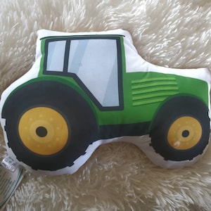May include: Green and yellow tractor-shaped cushion. The cushion is made of soft fabric and has a white background.