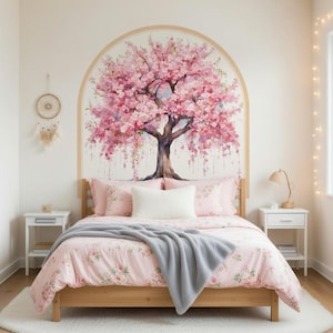 May include: A wall decal featuring a large cherry blossom tree with pink flowers inside a tan archway, positioned above a wooden bed frame with pink floral bedding, a white throw pillow, and a grey blanket, flanked by two white nightstands.